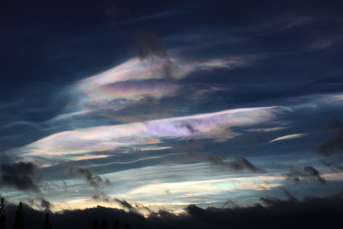 Pastellinsävyisiä helmiäispilviä korkealla ilmakehässä noin 15-30 kilometrin korkeudessa. Etualalla harmaan- ja tummansävyisiä alapilviä. 