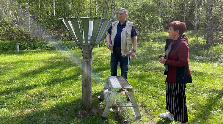 Havainnontekijä ja Ilmatieteen laitoksen havaintoyksikön edustaja katsovat sademittalaitetta nurmialueella.