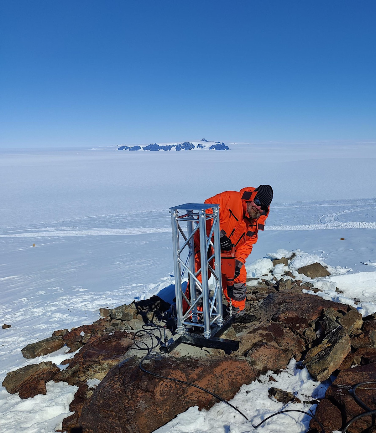 Jyri Näränen pystyttämässä satelliittiheijastimen mastoa kalliolle. 