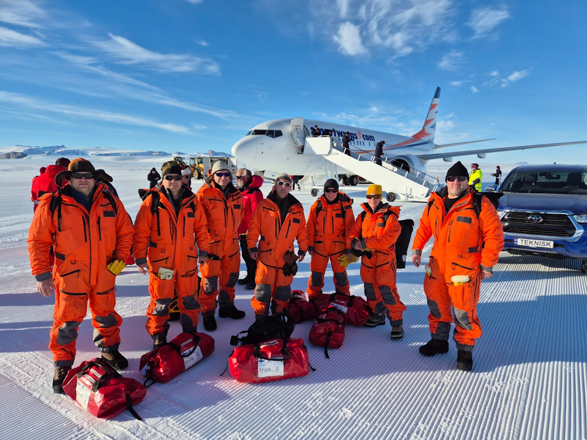 Retkikunnan jäsenet oransseissa haalareissa lentokoneen edustalla Etelämantereella.