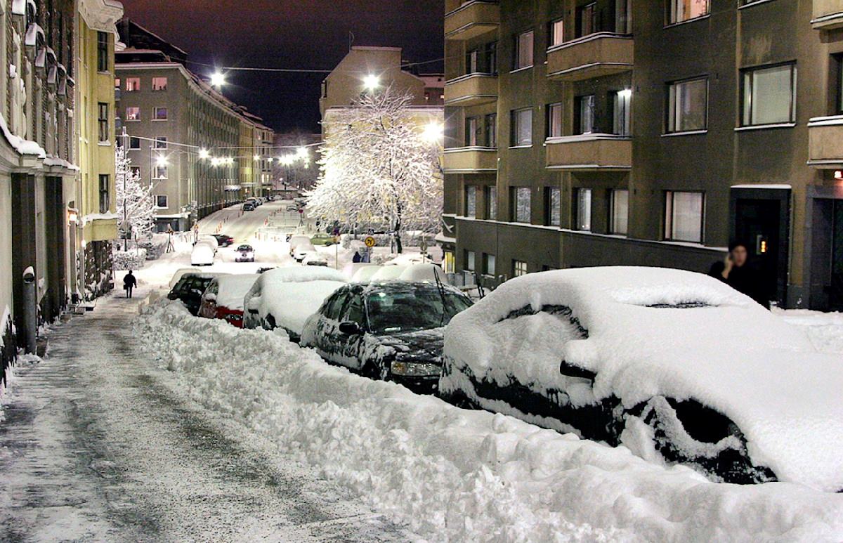 Talvinen risteys Helsingin Töölössä, jalkakäytävä hiekoitettu ja autot lumen peitossa.