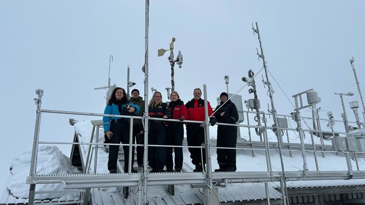 Haalariasuisia ihmisiä tutkimusaseman kattotasanteella, antenneja ja luminen katto.
