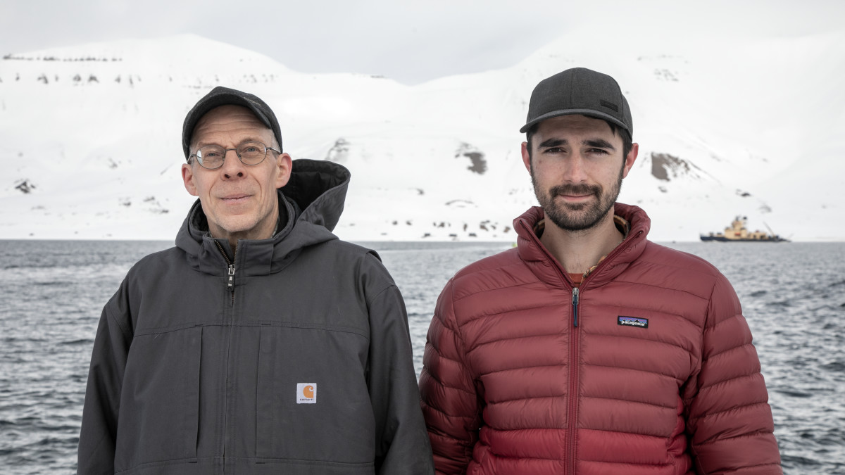 Tutkimusprofessori Timo Vihma ja väitöskirjatutkija Gabin Urbancic seisovat rannalla. Taustalla näkyy jäänmurtaja Oden.