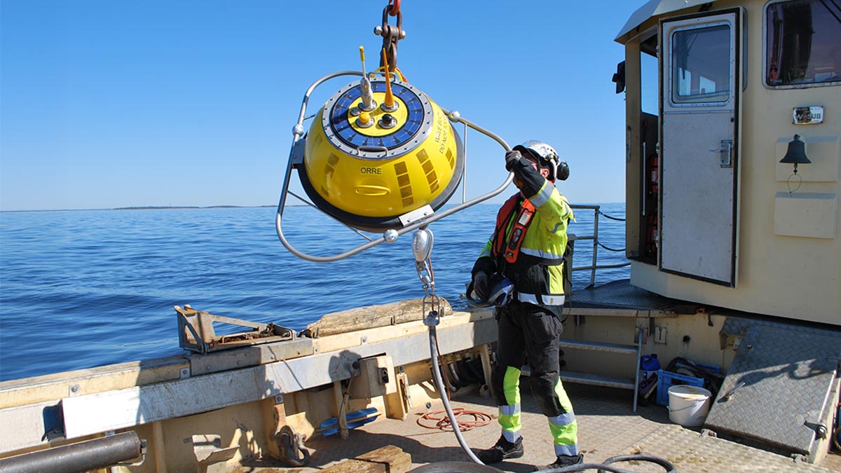 Työasuun pukeutunut mies ohjaa nosturin varassa olevaa poijua laivan kannelta merelle.