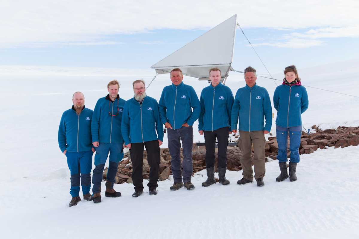 Ryhmäkuva FINNARP 2023 retkikunnasta satelliittiheijastimen edessä. 