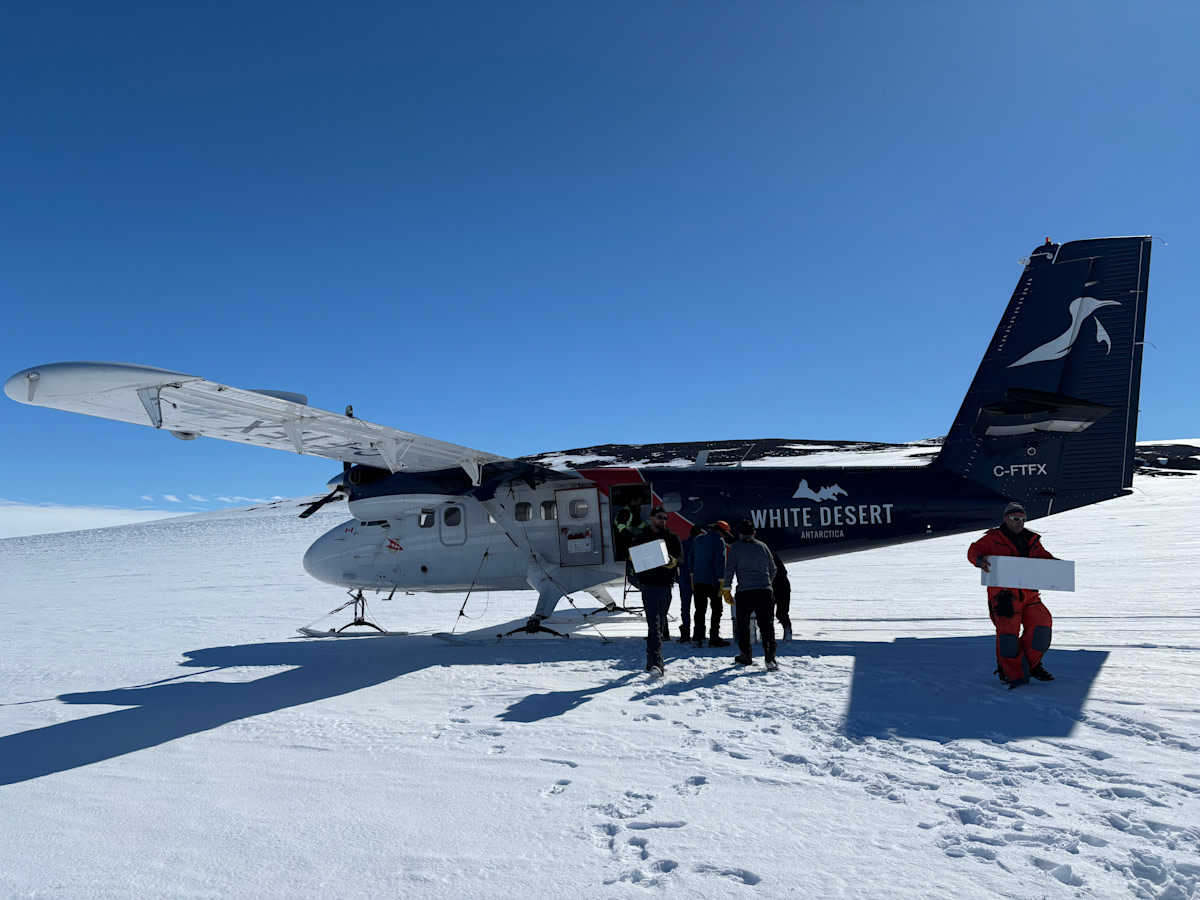 Suksilentokone laskeutuneena jäätikölle. Lastia puretaan koneesta.