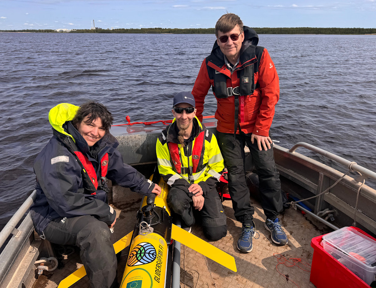Kolme henkilöä veneessä mittalaitteen kanssa.