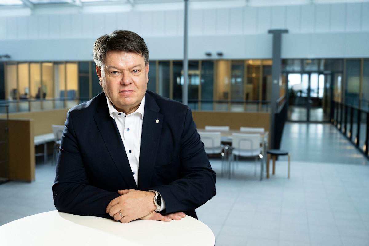 Henkilö katsoo kameraan, kädet pöydän päällä. Kuva on otettu sisätiloissa, Dynamicum-toimitalossa.