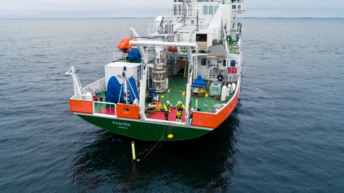 Tutkimusalus Arandan perässä kaksi turvapukuista ihmistä nostaa köydellä poijuja merestä.