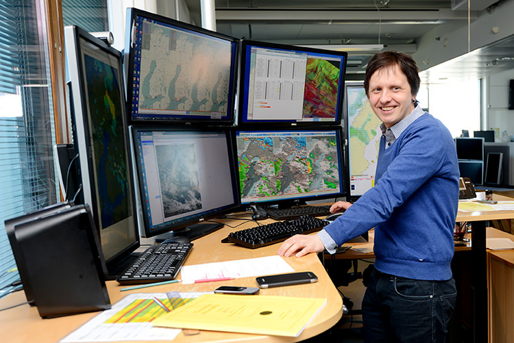 Meteorologi Anssi Vähämäki seisoo työpöydän ääressä Ilmatieteen laitoksen sääpäivystyksessä.
