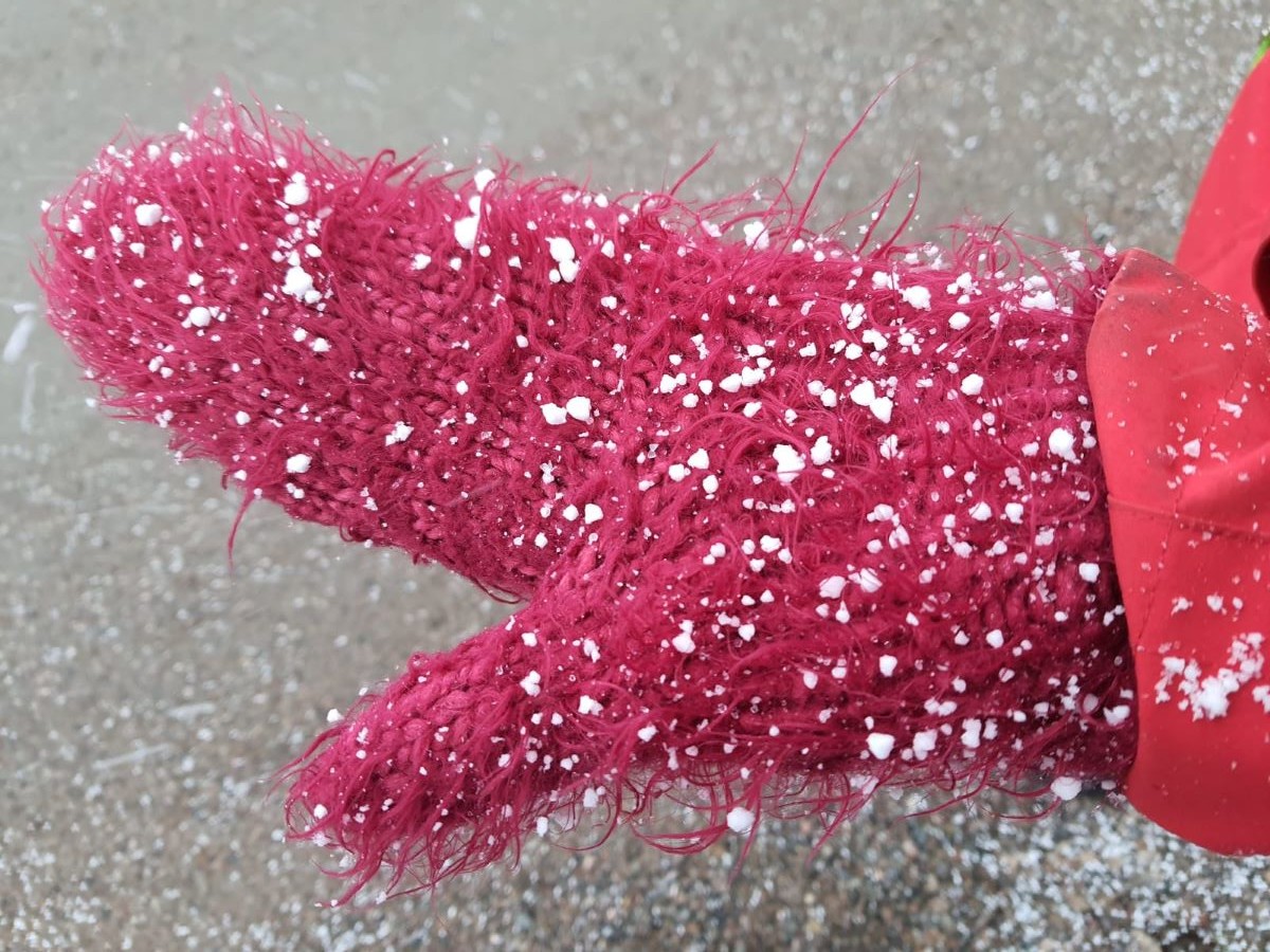 Erikokoisia ja vähän erimallisia lumirakeita punaista lapasta vasten.