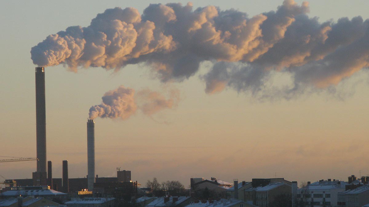 Talvinen kaupunkimaisema, jossa korkeista piipuista kaartuu vaakatasoiset vanat taivaalle.