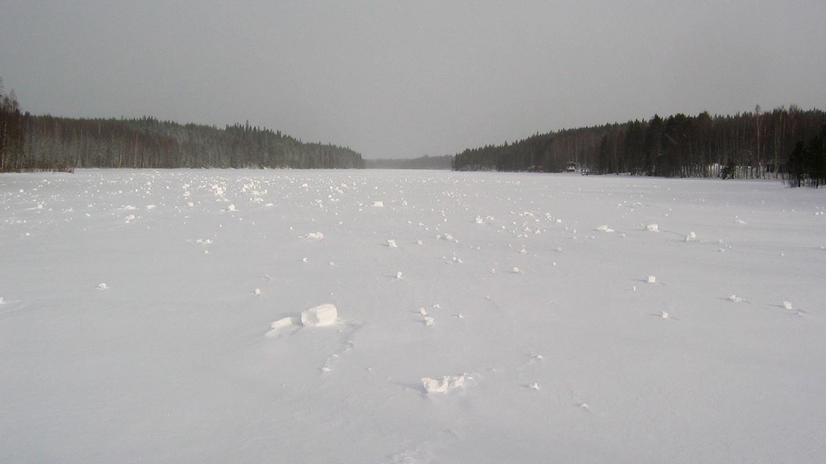 Erikokoisia lumirullia jäätyneen järven jäällä horisonttiin saakka.