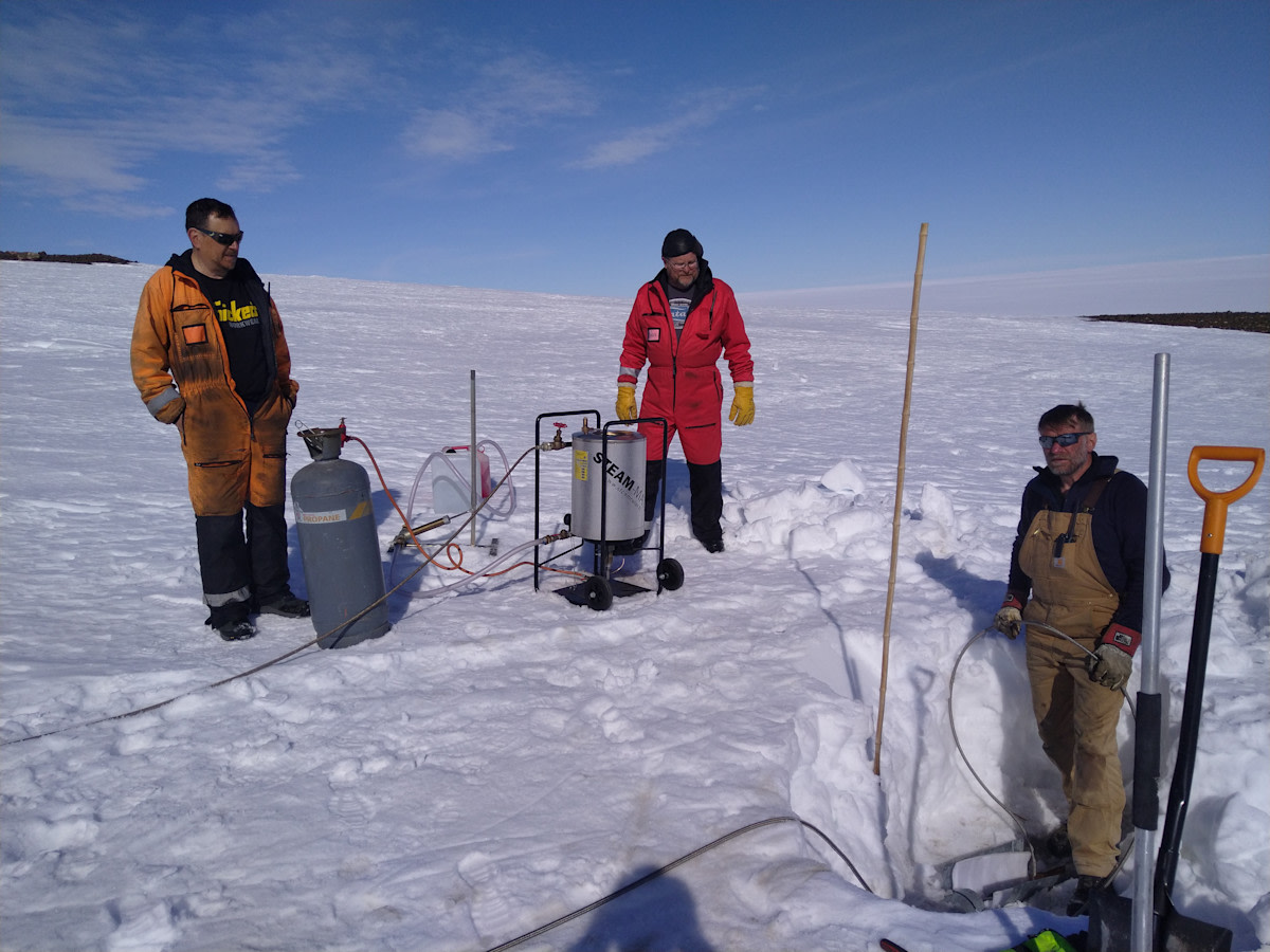 Kolme miestä työhaalareissa jäätiköllä hyödynkehittimen kanssa. Kuva Mika Kalakoski/FINNARP.