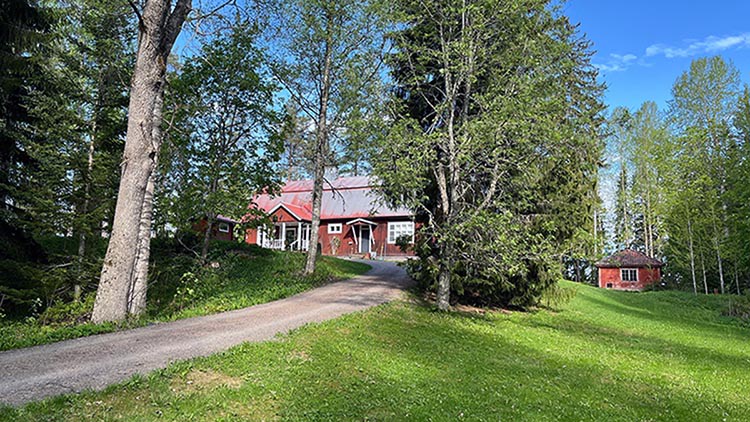 Tilanhoitajan punamultainen talo näkyy puiden takana puistomaisemassa.