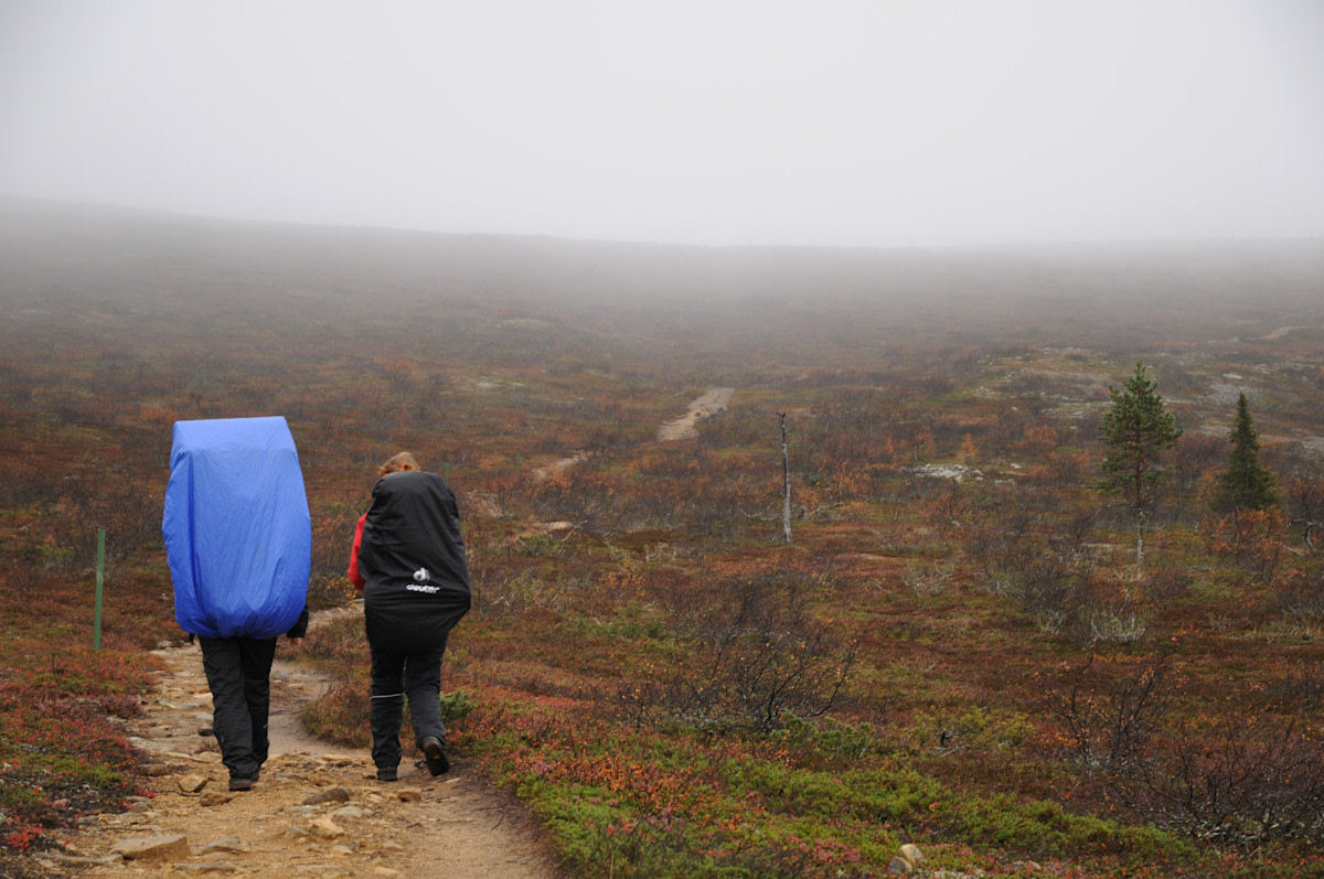 Kaksi retkeilijää kävelemässä ylös kivistä polkua syksyisessä ja sumuisessa tunturissa.