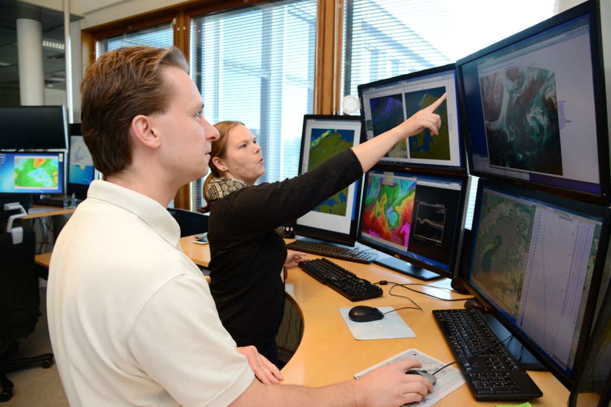 2 päivystävää meteorologia lukuisan määrän näyttöjä edessä pohtimassa sääennustetta yhdessä.