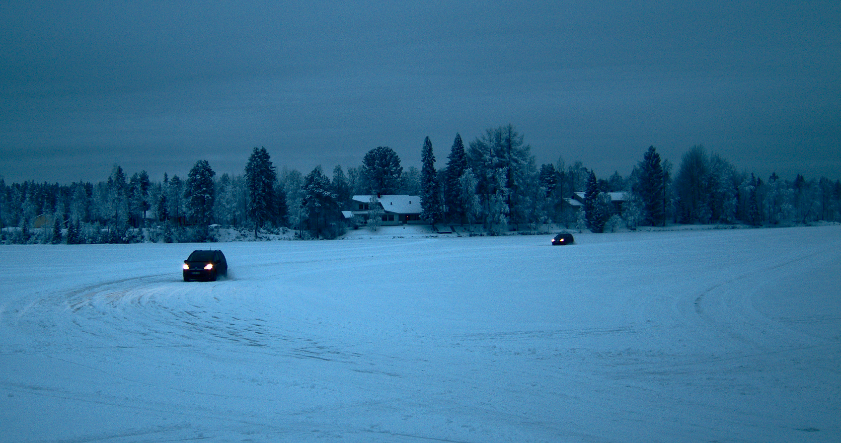 Kaksi autoa ajaa hämärässä jään päällä.