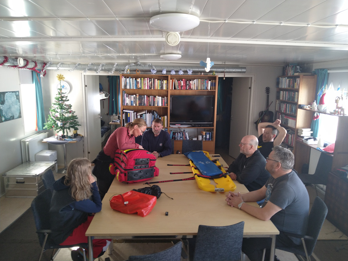 Retkikunta pöydän ääressä tutustumassa lääkintävarusteisiin lääkärin johdolla.